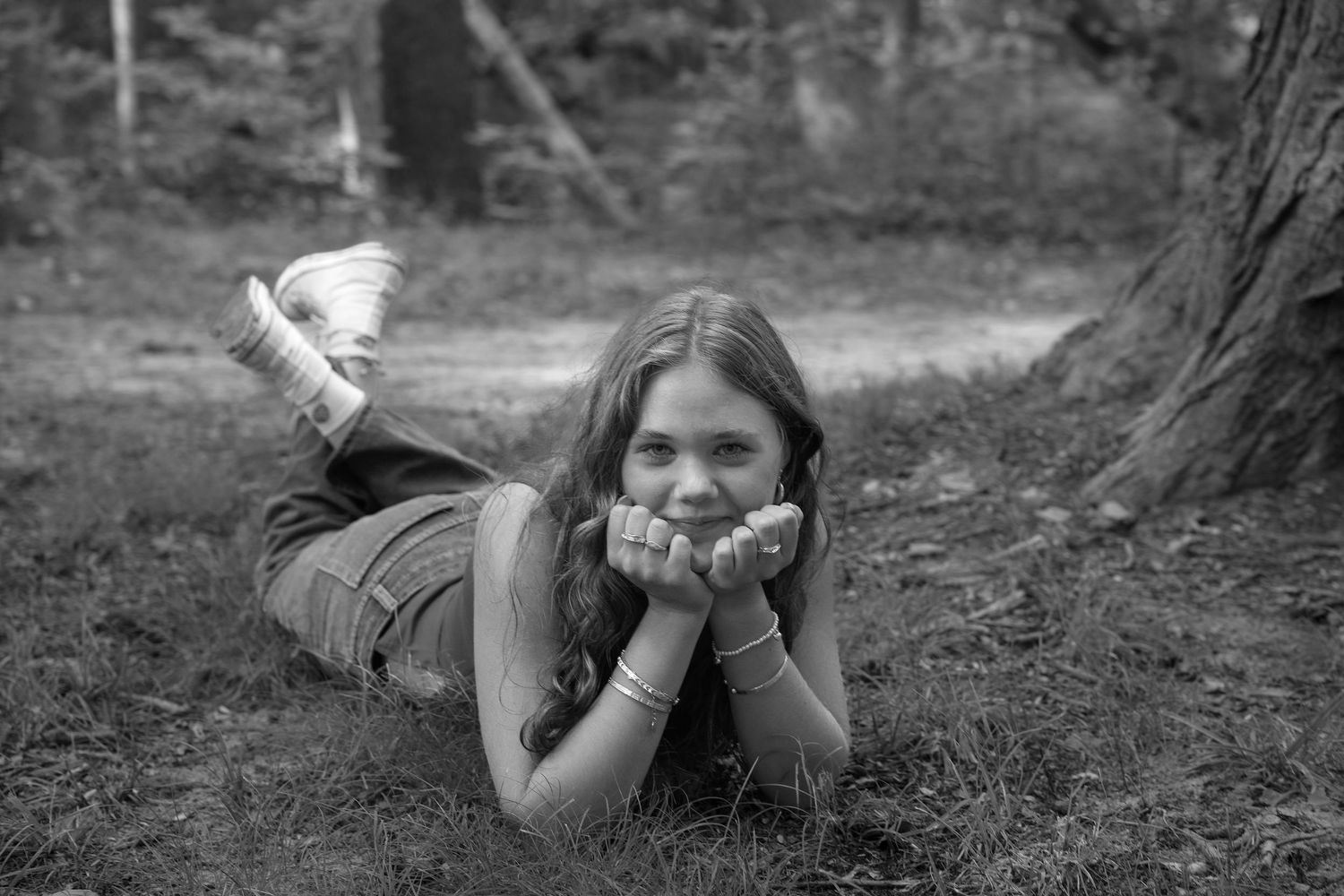 A sequence of black and white photos showing someone lying on the ground in a forest taking photographs.