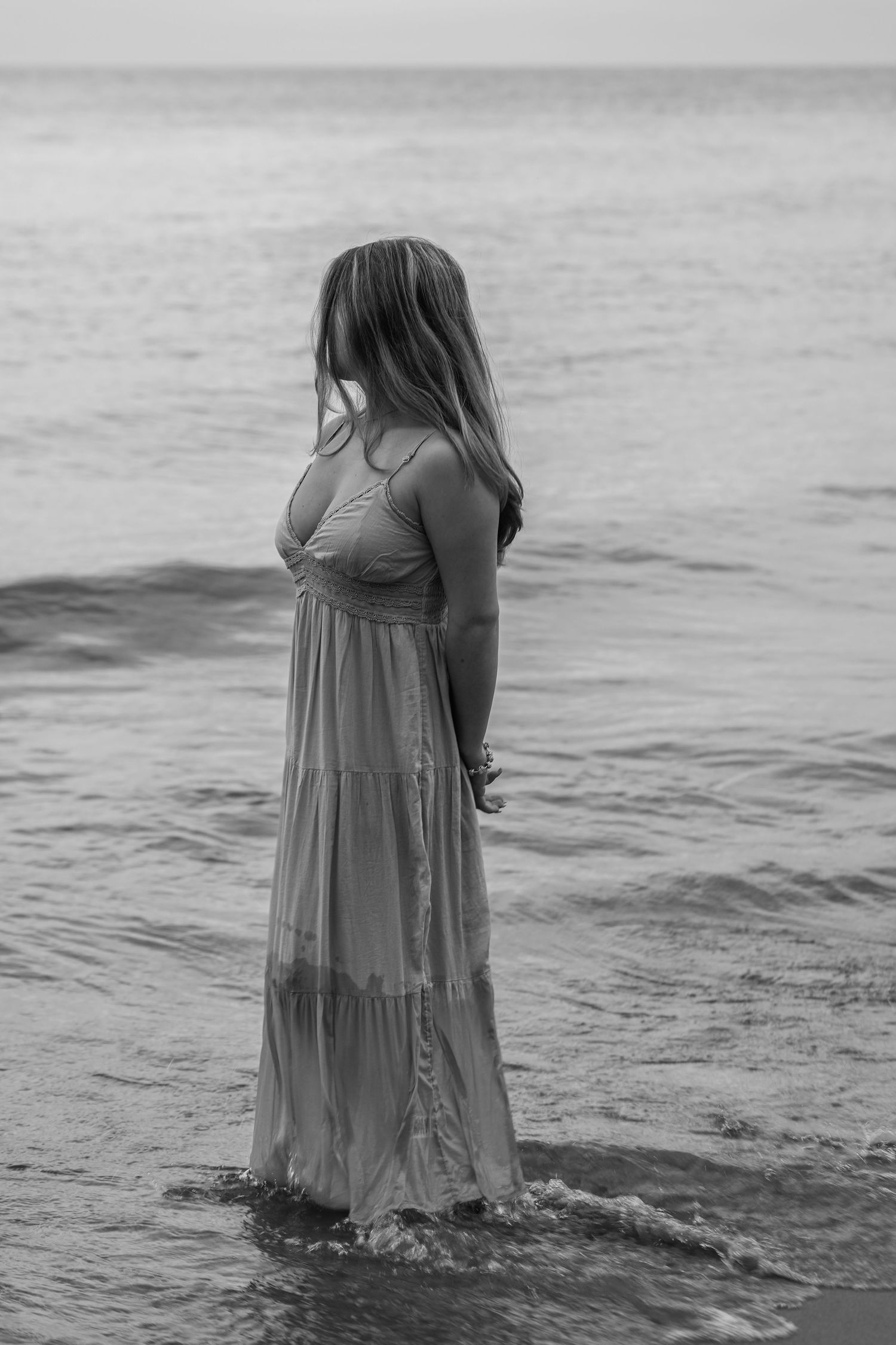 A black and white photo series shows a person in a flowing dress wading deeper into ocean waves.