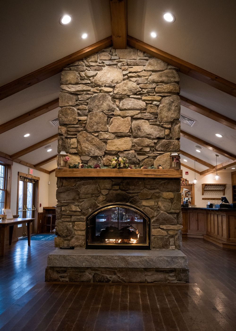 Rustic stone fireplace with wood mantel in elegant venue with vaulted ceiling and hardwood floors.