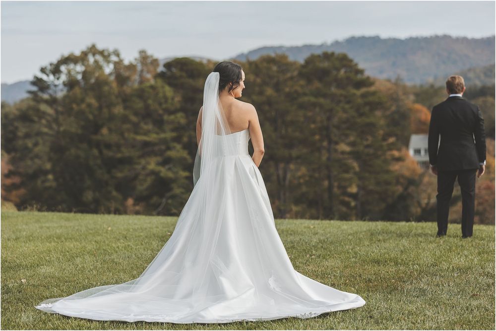 A bride and groom stand together on a grassy hillside during their outdoor wedding ceremony at sunset.