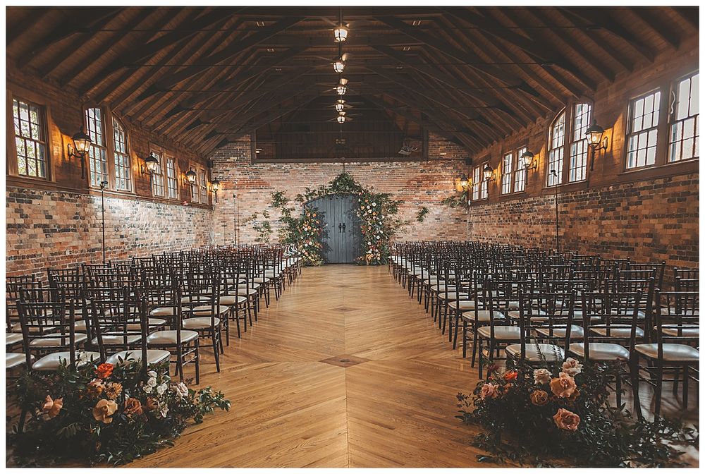 Panoramic view of a rustic wedding venue with exposed brick walls, wooden beams, and rows of dark chairs.