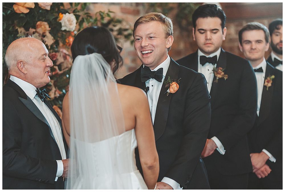 Wedding ceremony with couple exchanging vows surrounded by wedding party members in formal attire.
