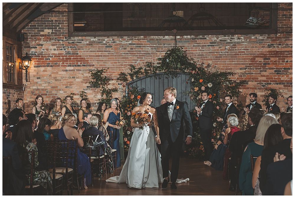 Wedding guests celebrate on a dance floor in front of exposed brick walls at an indoor reception venue.
