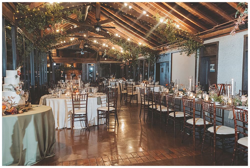 Elegant wedding reception setup in a spacious barn venue with long tables, string lights and natural decor elements.