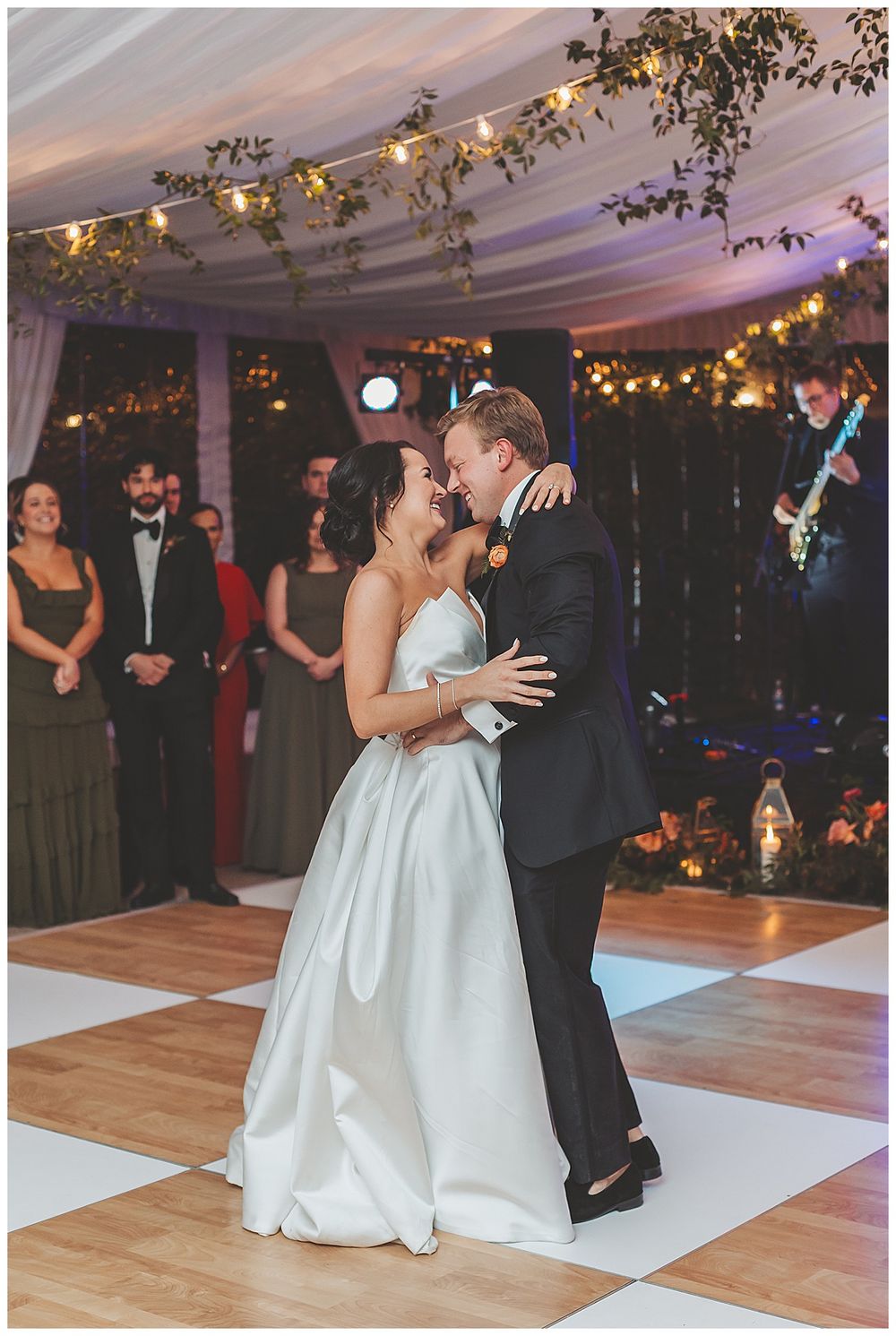 A couple shares a romantic dance sequence on a white dance floor under twinkling lights at an elegant wedding reception.