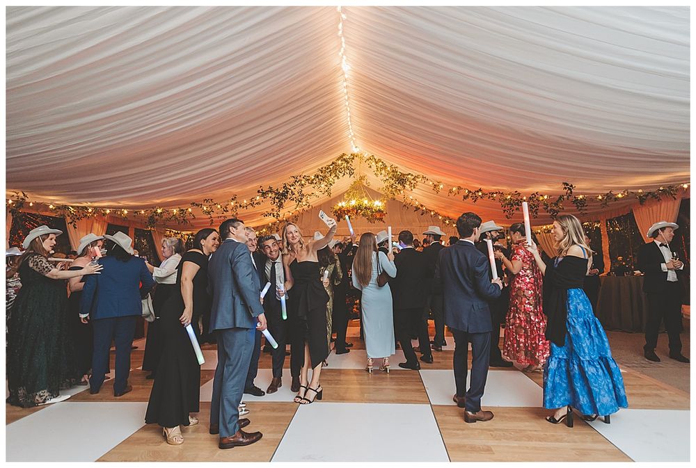 Elegant white tent reception venue with string lights and guests dancing on wooden floor.