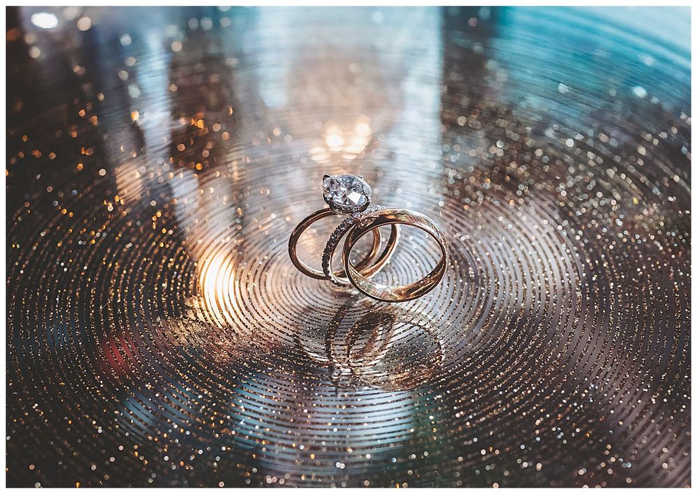 Wedding rings sparkle on a reflective surface with bokeh lights creating a magical, romantic atmosphere.