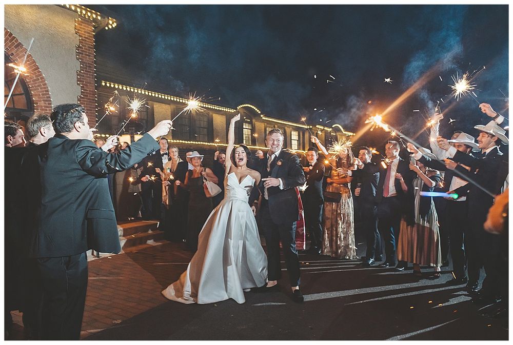 Wedding party sparkler exit photos showing guests creating a glowing tunnel as couple departs at night.