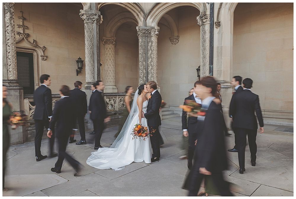 Formal wedding portraits being taken under ornate stone archways and columns of a historic building.