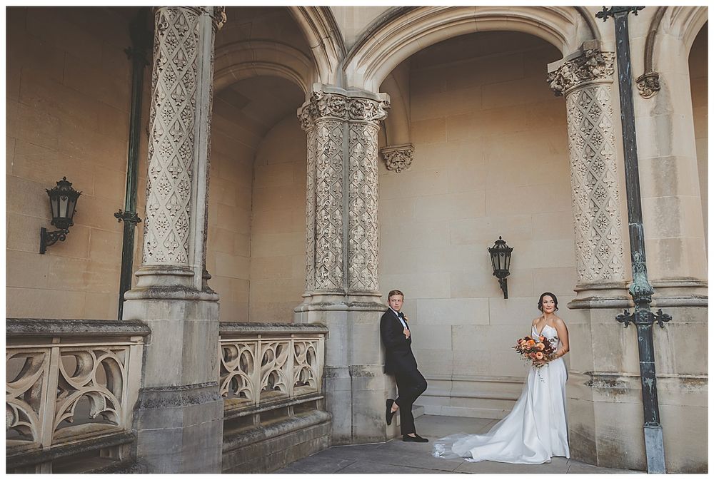 A bride walks along an elegant stone colonnade with arched architecture and decorative pillars in the background.