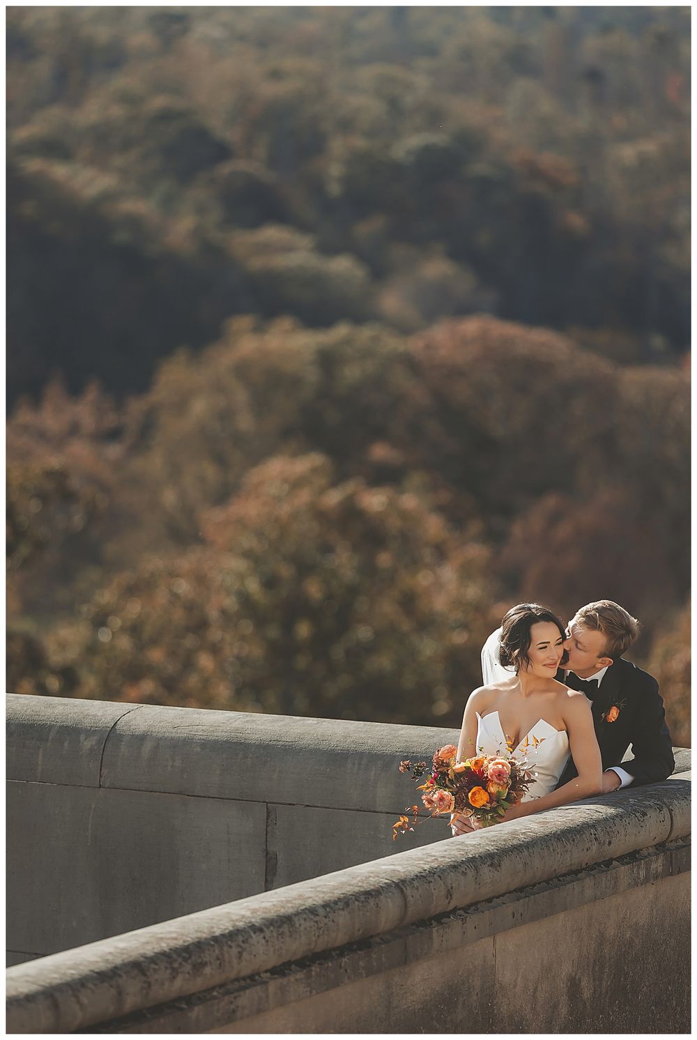 Romantic autumn wedding photo session along a stone wall overlooking mountain scenery.