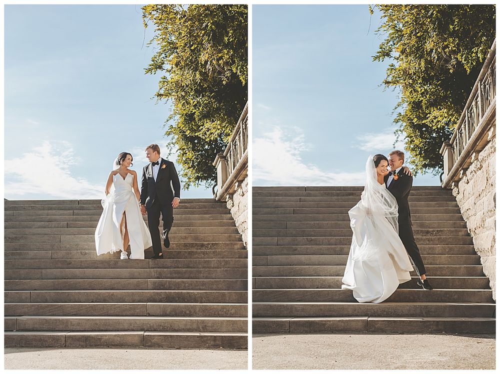 Wedding couple descends grand stone staircase outdoors with bride's dress flowing in the breeze.