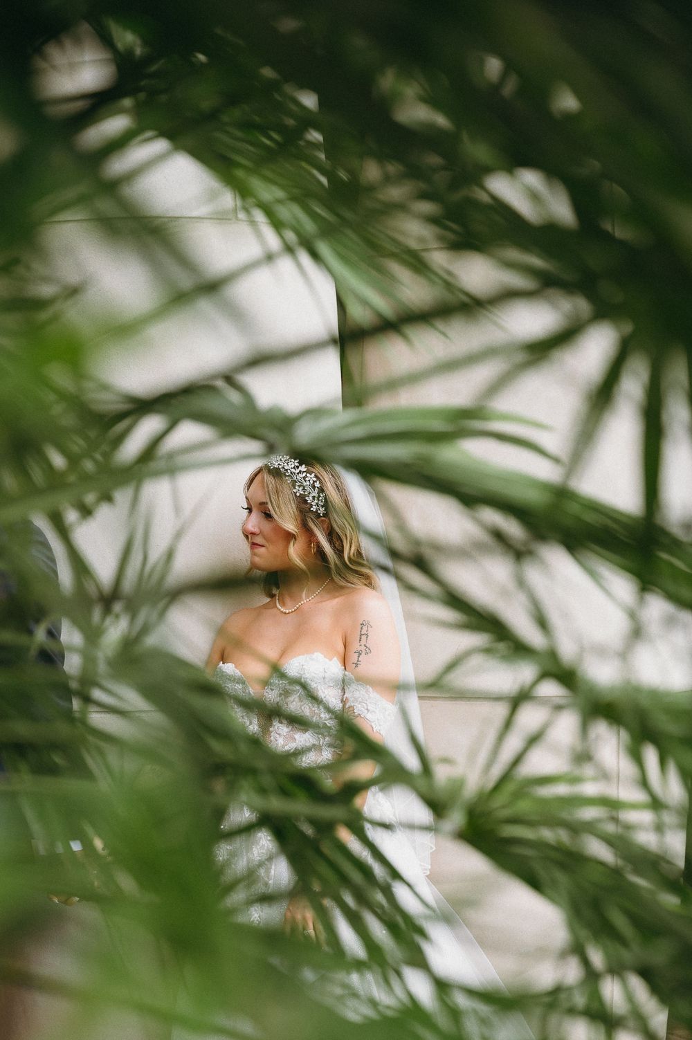 Artistic portrait of bride in white dress framed through tropical palm leaves.