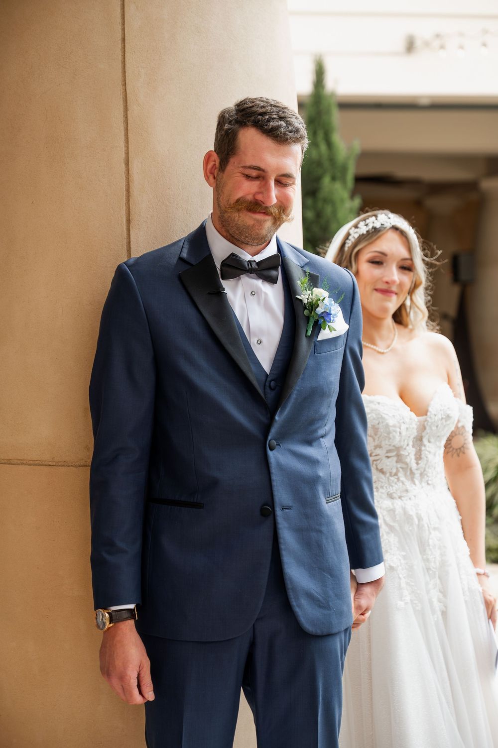 Wedding couple shares joyful first look moment in elegant columned setting.