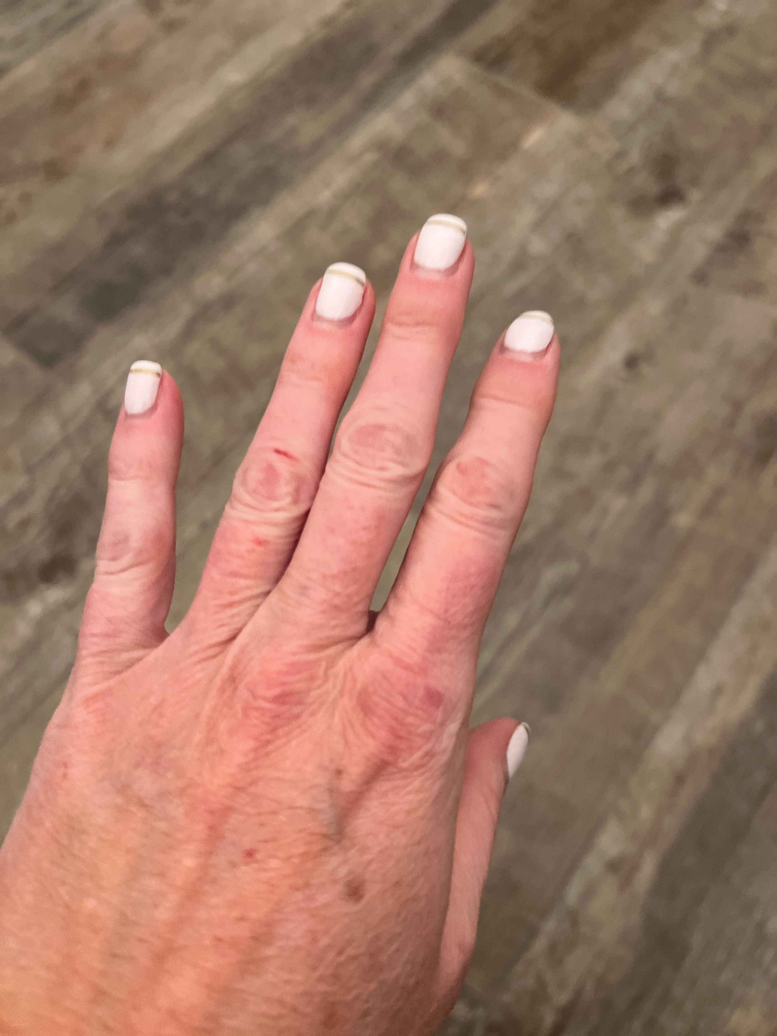 Close-up view of manicured fingernails with alternating white and gray polish on a textured surface.