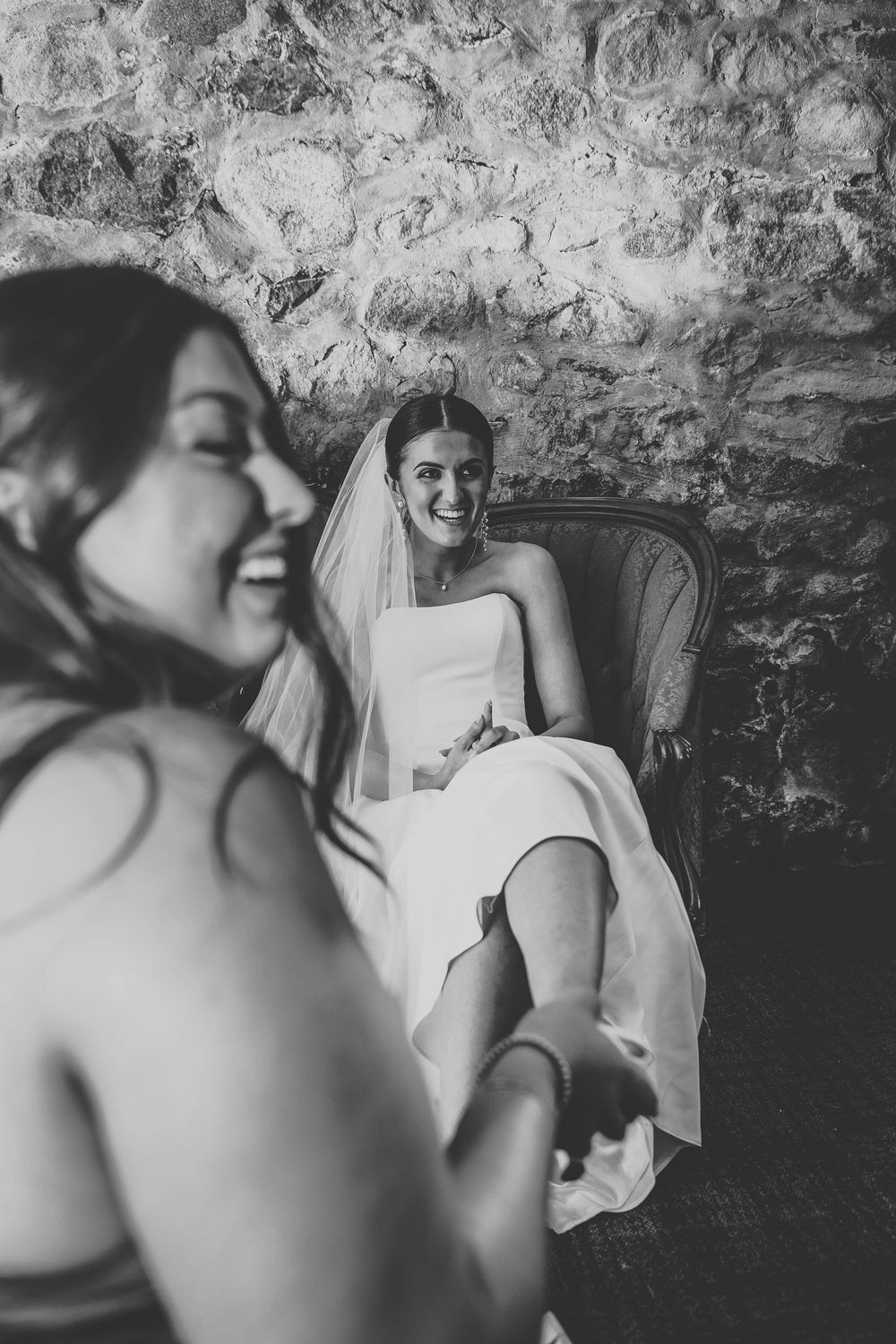The maid of honor helping the bride get her high heels on in the knights castle