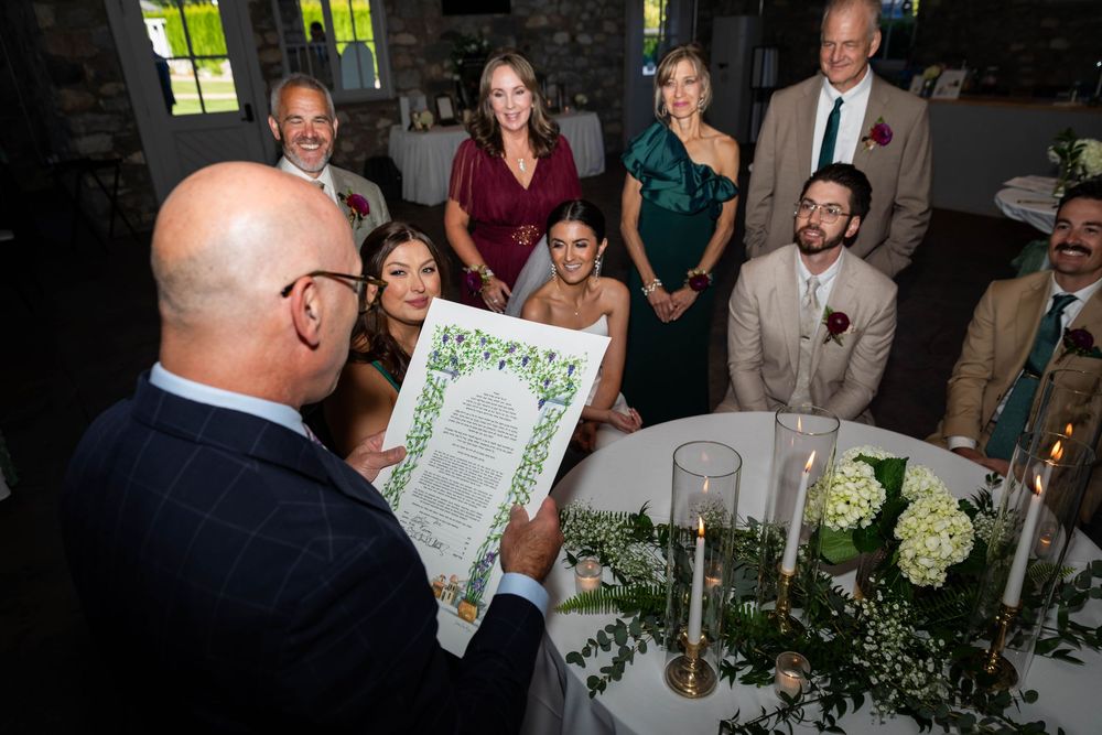 Wedding guests laugh and celebrate during a joyful reception moment around elegant table settings with greenery decor.