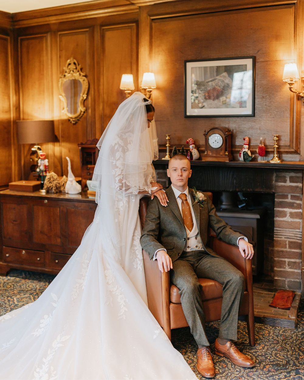 A wedding couple shares intimate moments in a warmly lit wood-paneled room with vintage furnishings and brick walls.