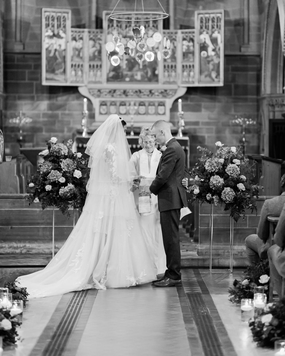 Black and white wedding ceremony photos showing a couple at the altar with floral arrangements in a church setting.