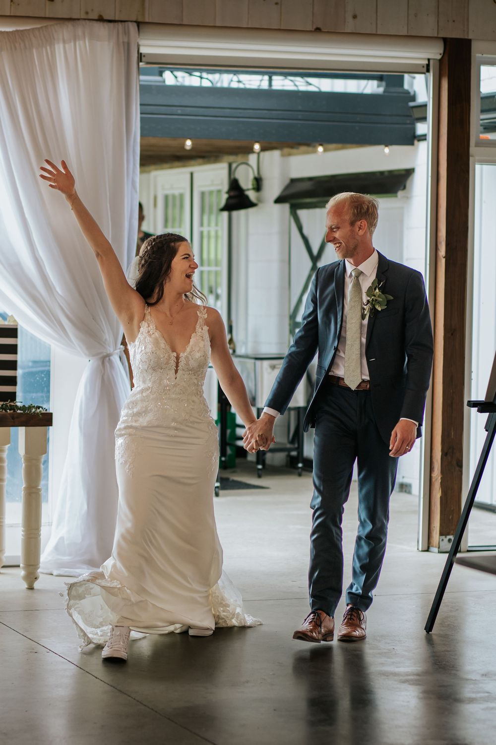 Wedding couple dancing and twirling in an indoor venue with white curtains and concrete floors.