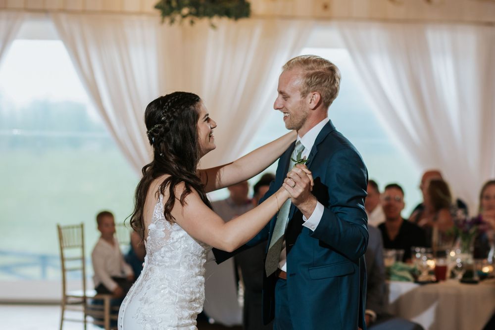 A couple shares their first dance at a wedding reception with white drapes and greenery decorations.