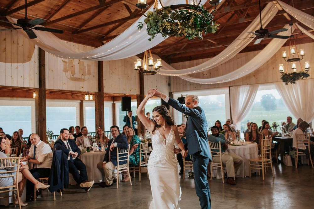 Couple dancing in rustic venue decorated with white drapes and hanging greenery.