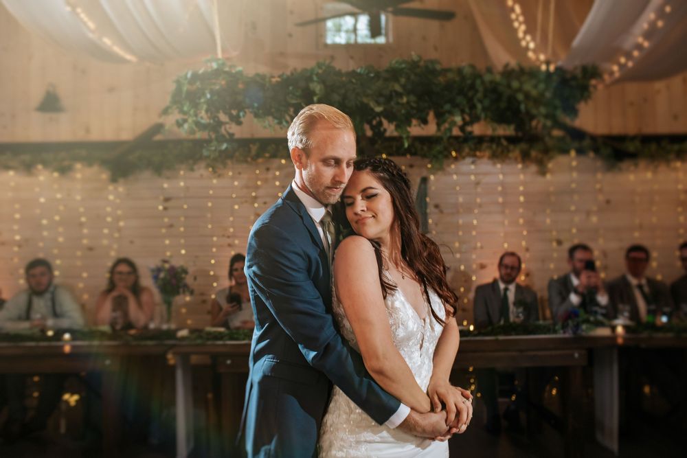 Romantic dance moment under twinkling lights at an elegant barn wedding reception.