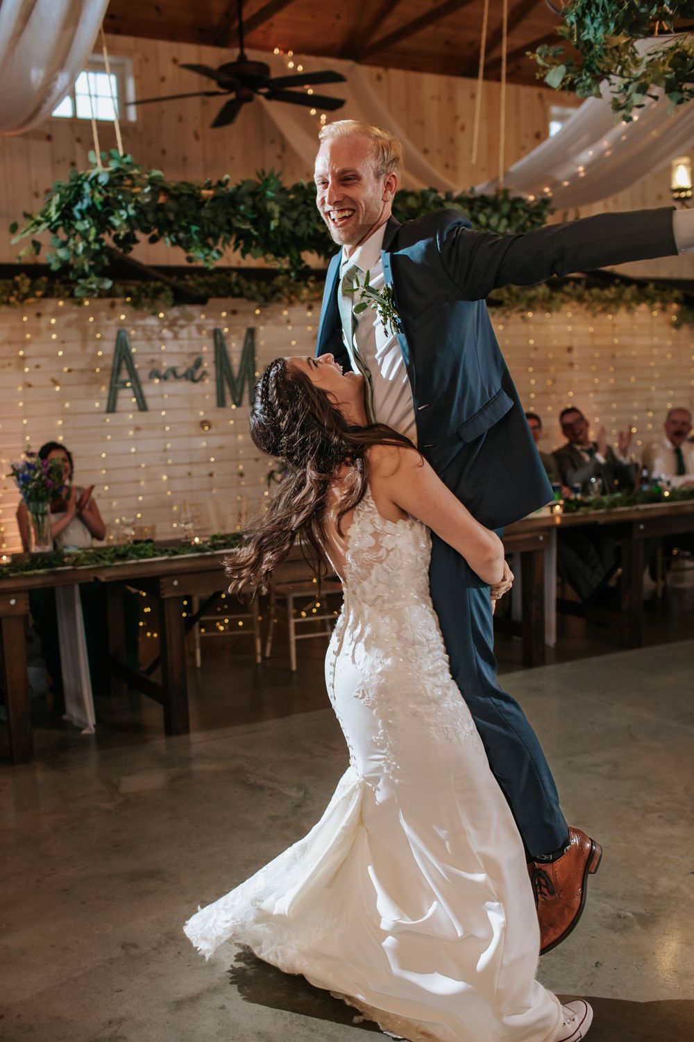 Energetic dance moves during wedding reception in rustic venue with string lights.