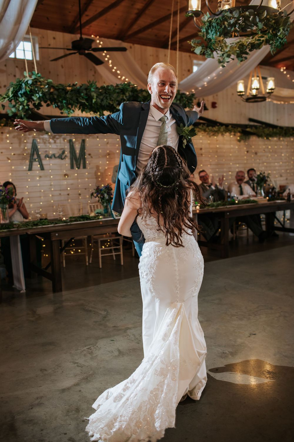 Lively dance moment at wedding reception with rustic barn backdrop and twinkle lights.