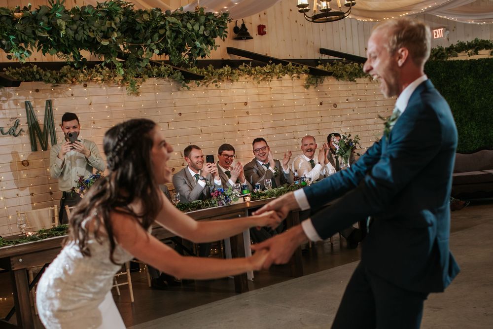 Playful dance moves at wedding reception with rustic decor and greenery.