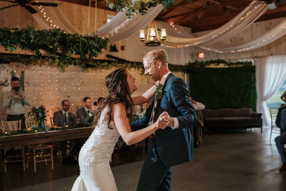 Couple sharing intimate dance moment in rustic venue with draped fabric and greenery.