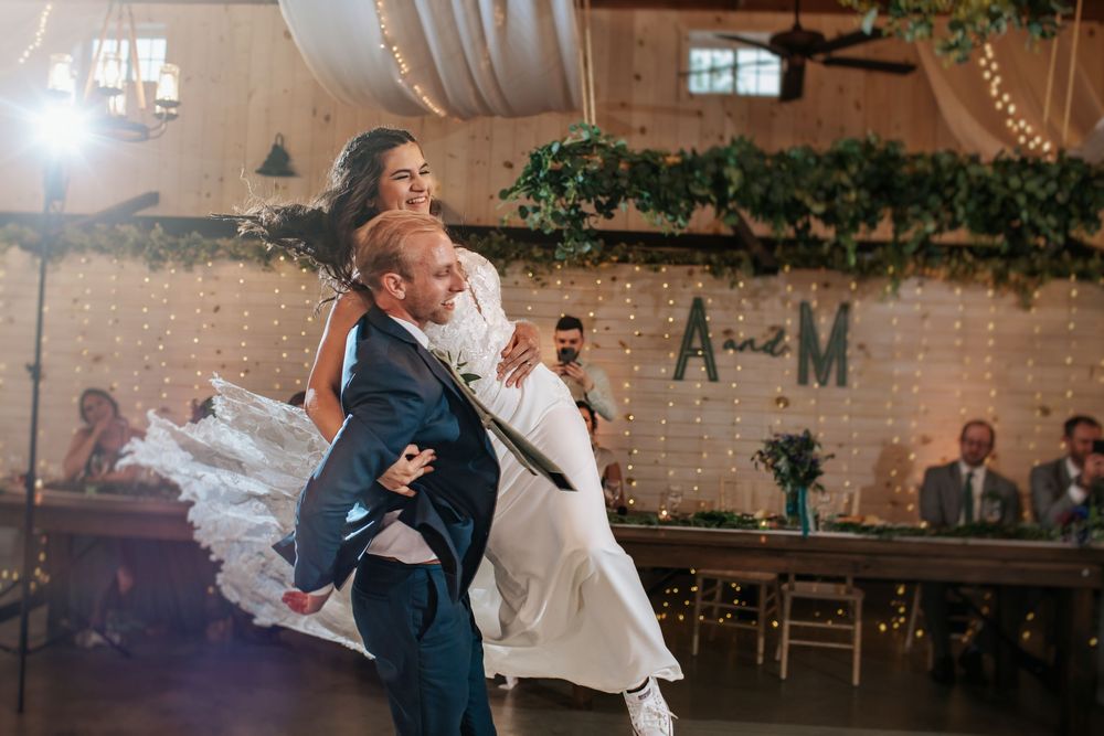 Couple performs an elegant dip during their first dance at a rustic wedding reception venue with string lights.