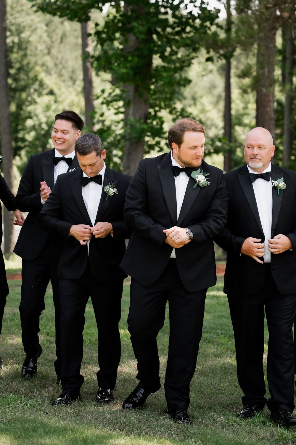 Groomsmen in black tuxedos share a lighthearted moment outdoors during wedding photos.