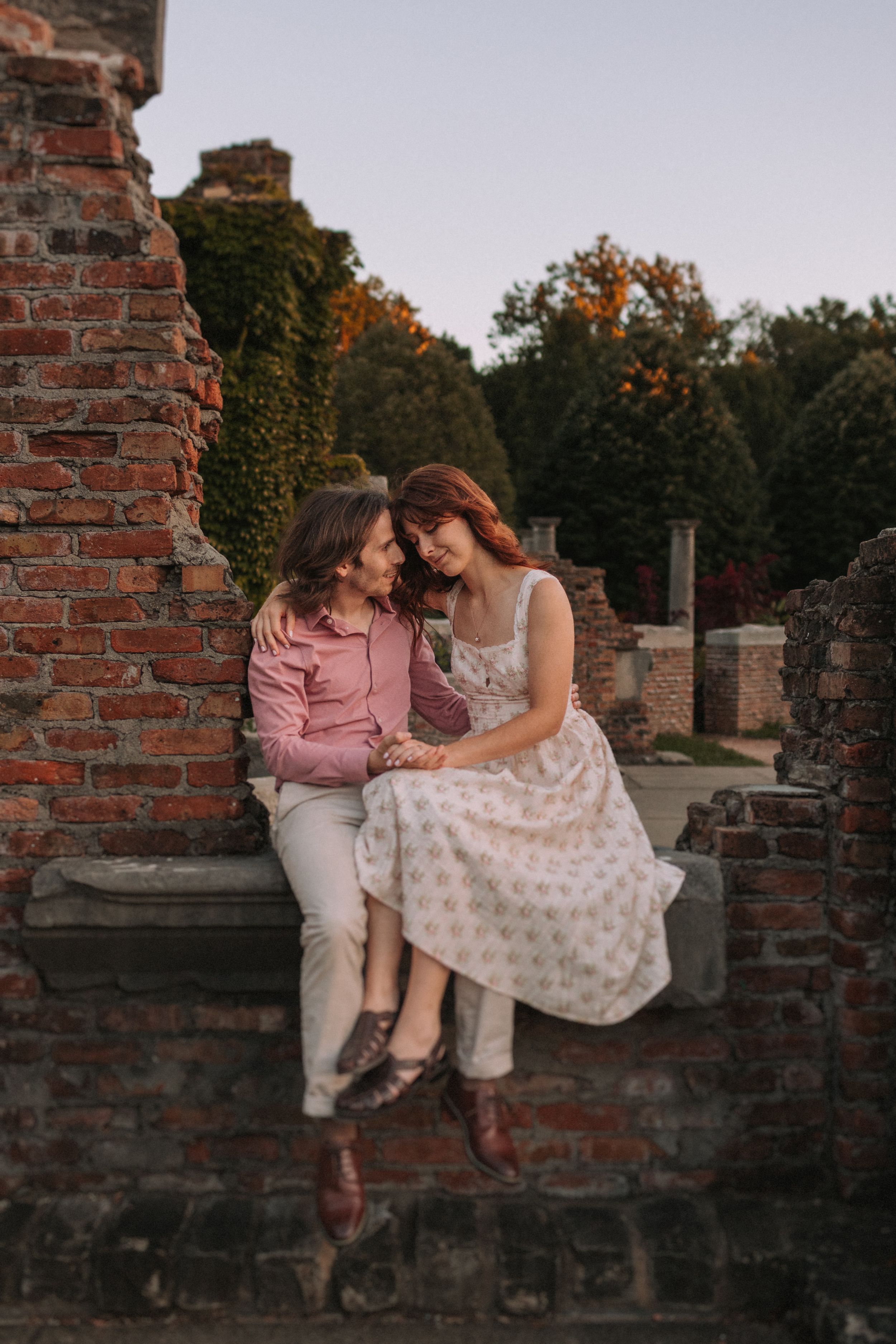 A couple sits intimately on an old brick wall during sunset.