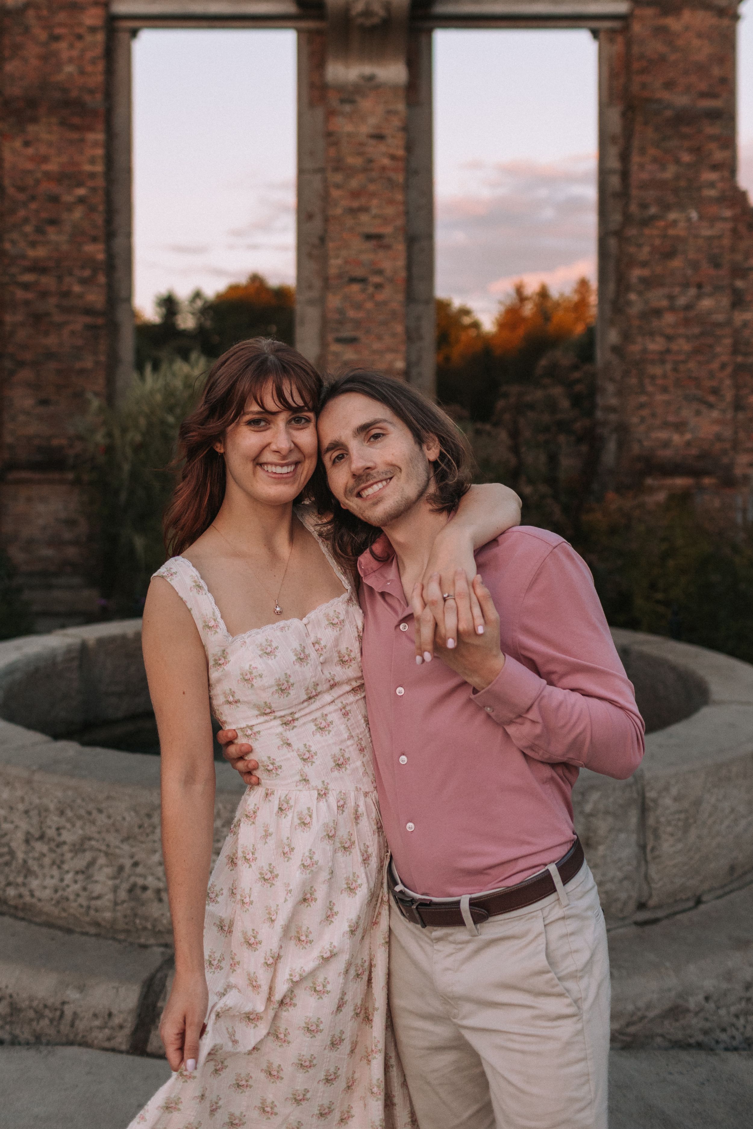 A joyful couple poses in front of brick ruins during sunset.