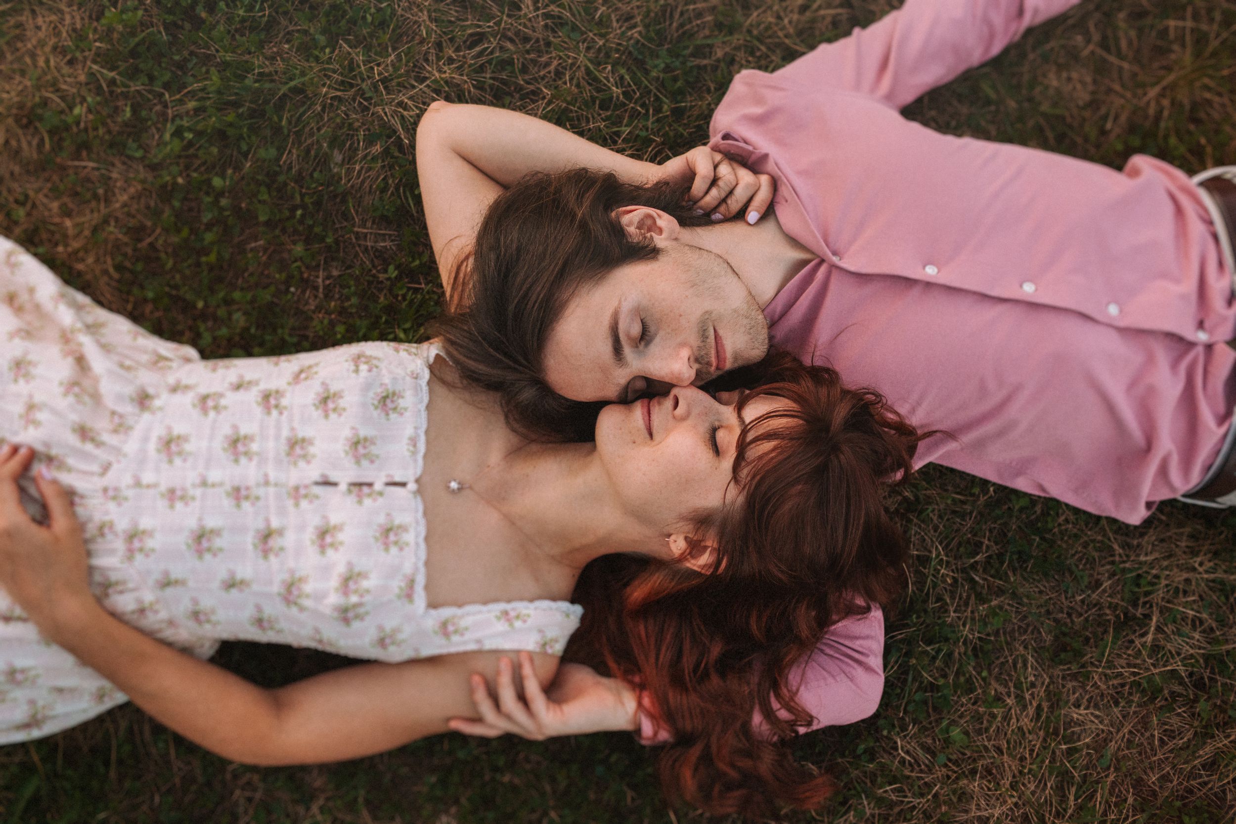 A person in pink and white clothing lies peacefully on grass in a dreamy outdoor setting.