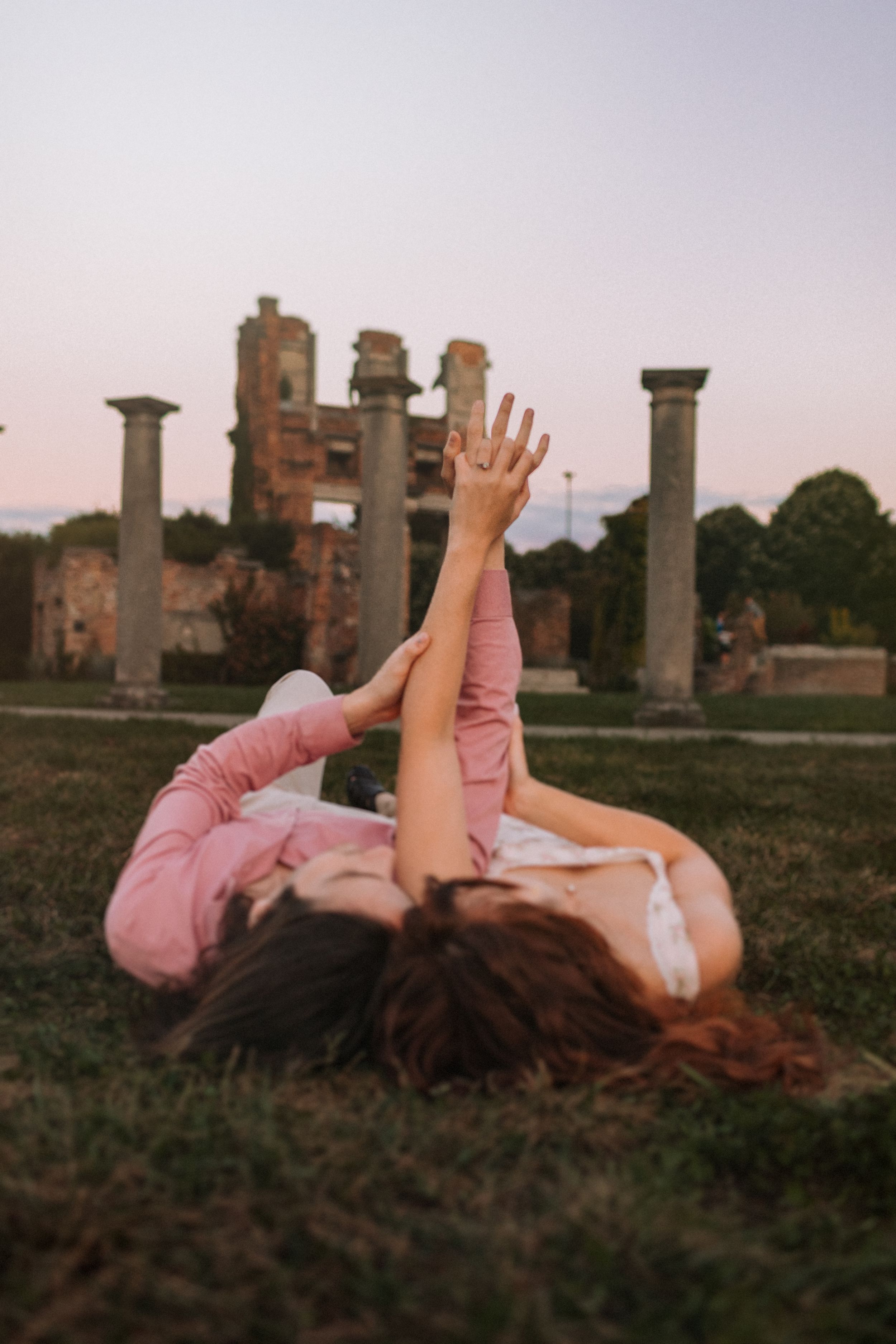 Couple lying on grass near historic ruins during sunset photoshoot.