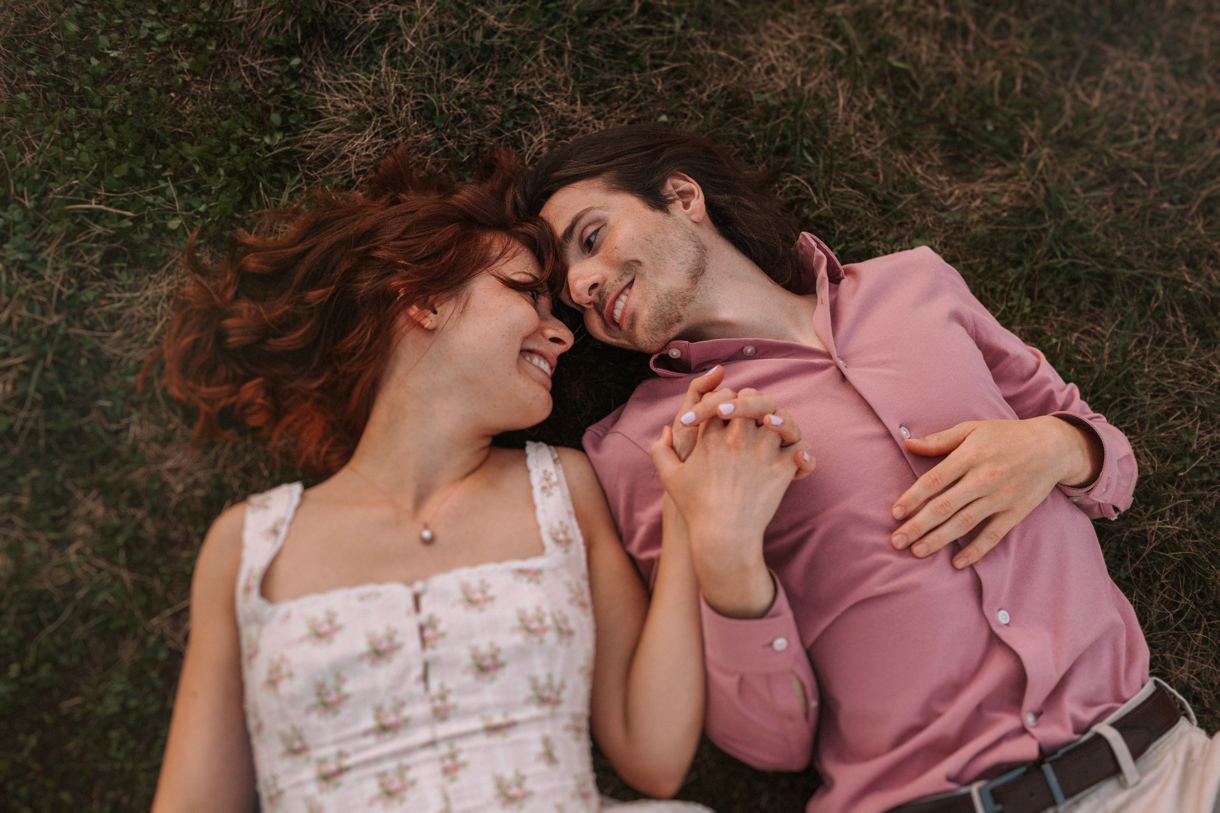 Couple sharing tender moments on grass with brick ruins in background.