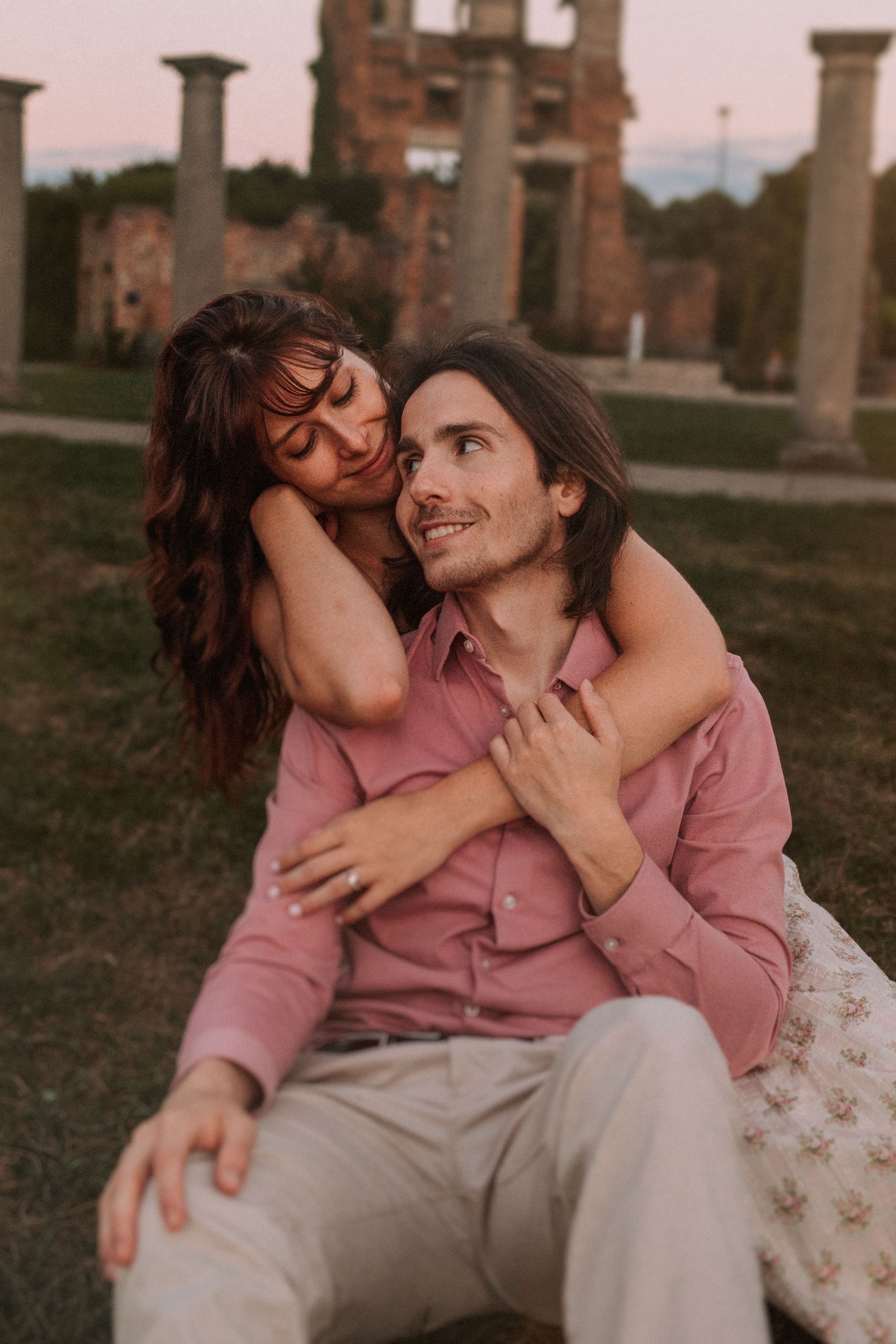 Intimate couple embracing on grass during sunset photo session near historic architecture.