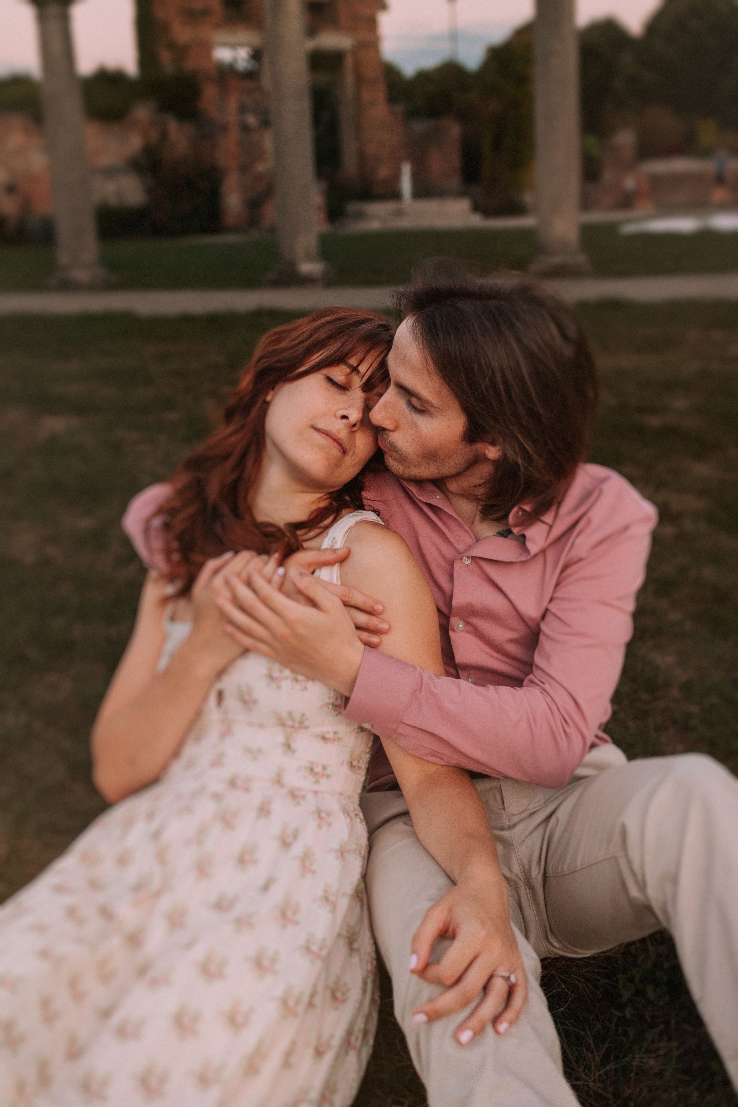 A romantic couple shares tender moments while sitting together on grass during sunset.