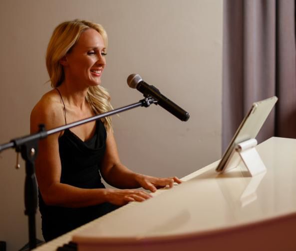 A chef in a black uniform smiles while standing in a professional kitchen setting.