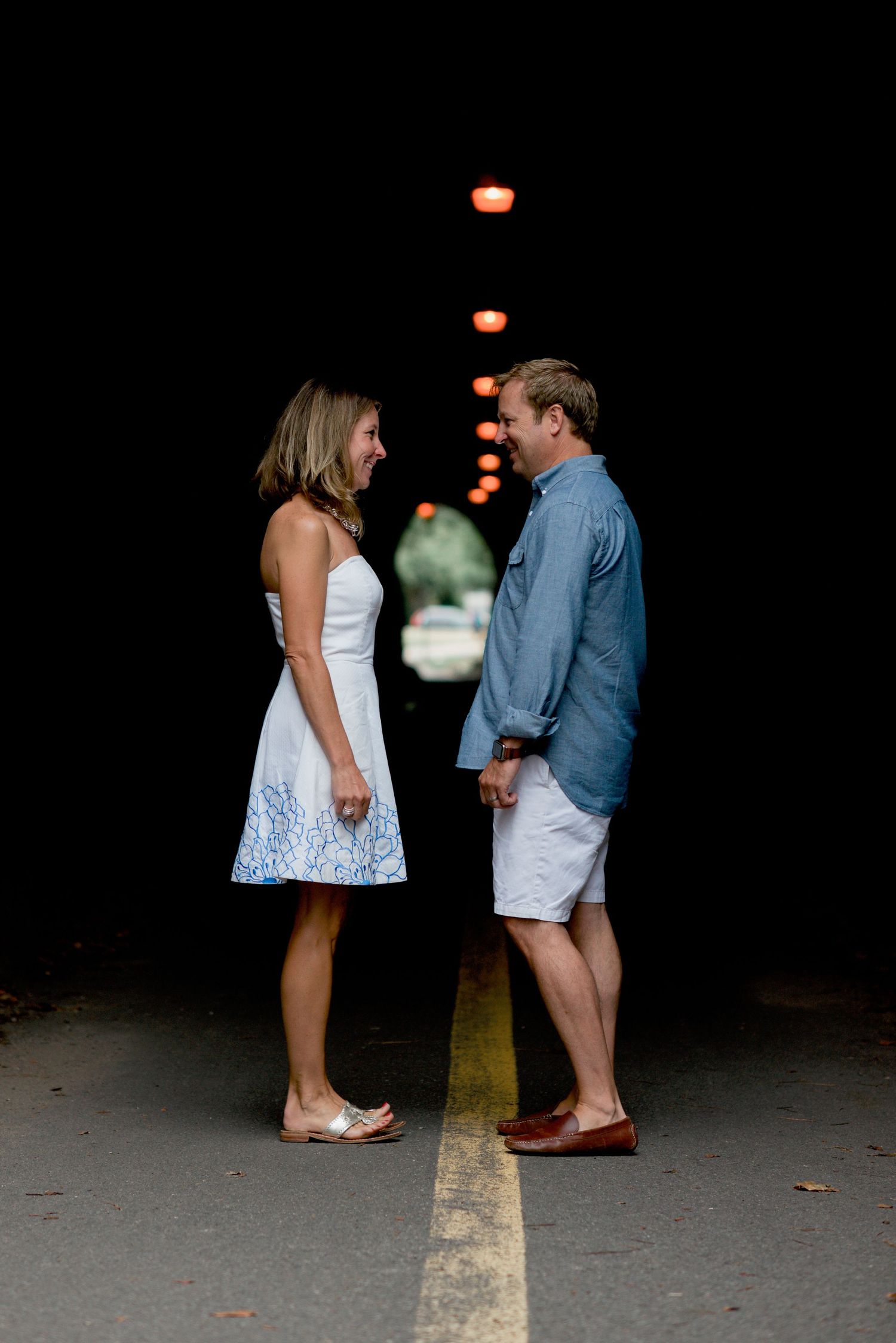 Couple in casual summer outfits standing together at night on yellow line.