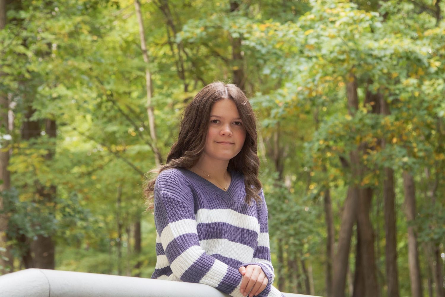 A person in a navy striped shirt walks through a lush green forest on a sunny day.