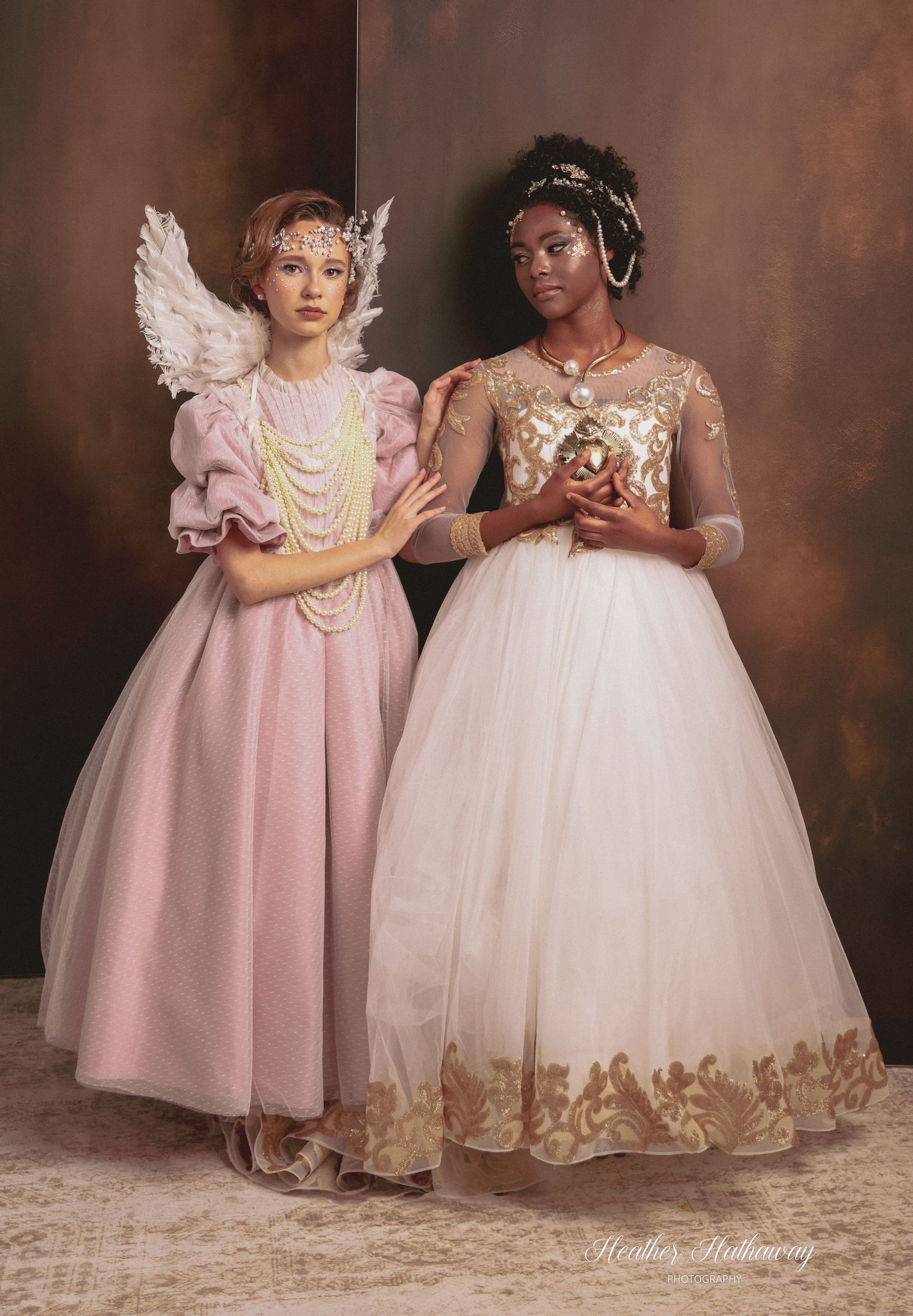 Two young children wearing elegant princess-style dresses in pink and cream colors pose together in a studio setting.