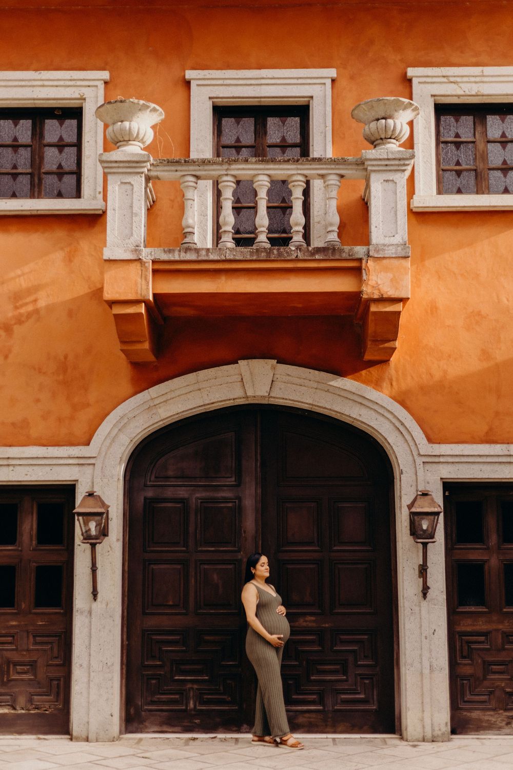 Architectural maternity photos against an orange stucco building with dark wooden doors.