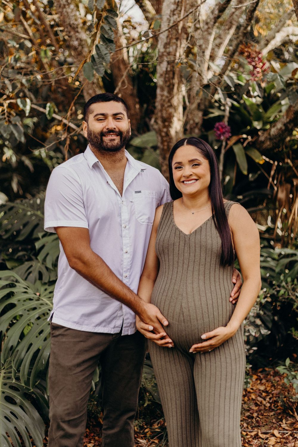 Maternity photoshoot in a lush garden setting with couple in coordinated casual outfits.
