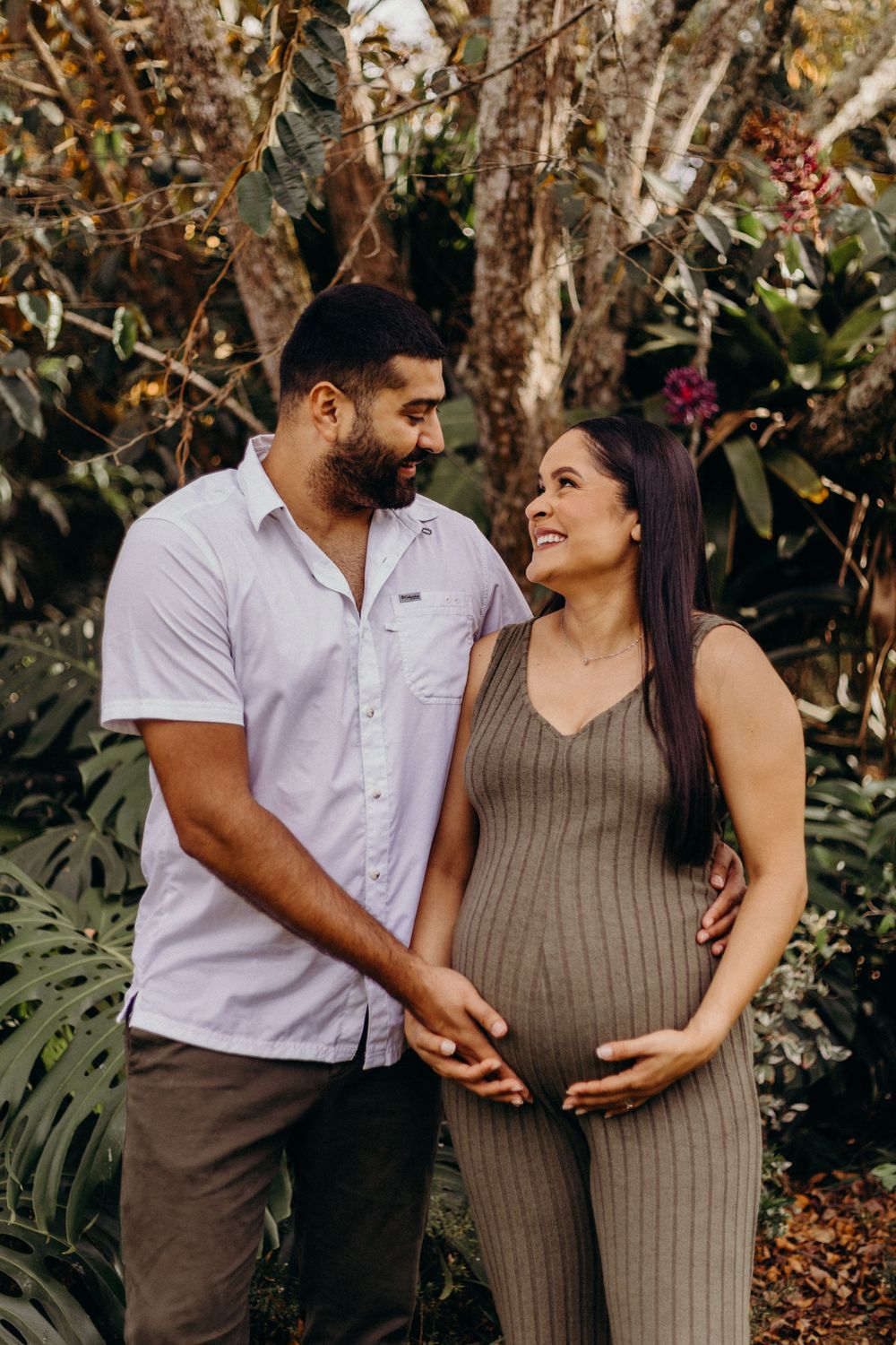 An expectant couple poses lovingly in a garden setting with natural lighting.