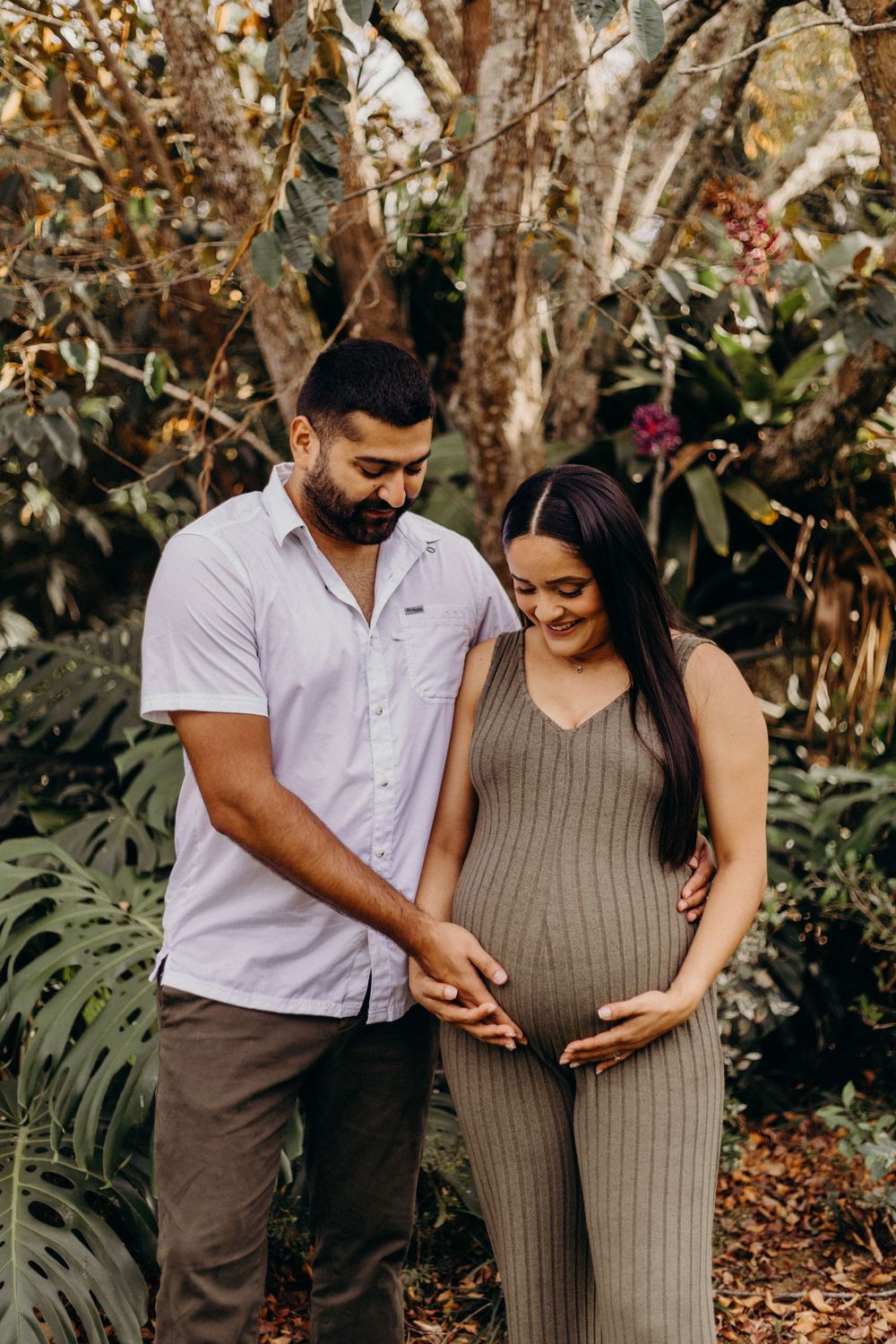 A couple shares tender moments during their pregnancy photoshoot among trees and foliage.