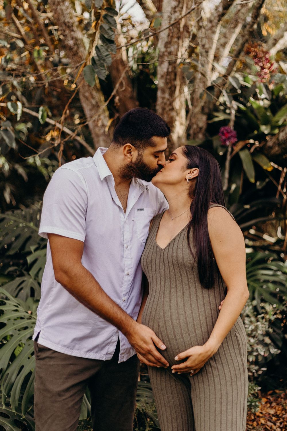 Romantic maternity photoshoot of expectant couple embracing in a garden setting with natural lighting.