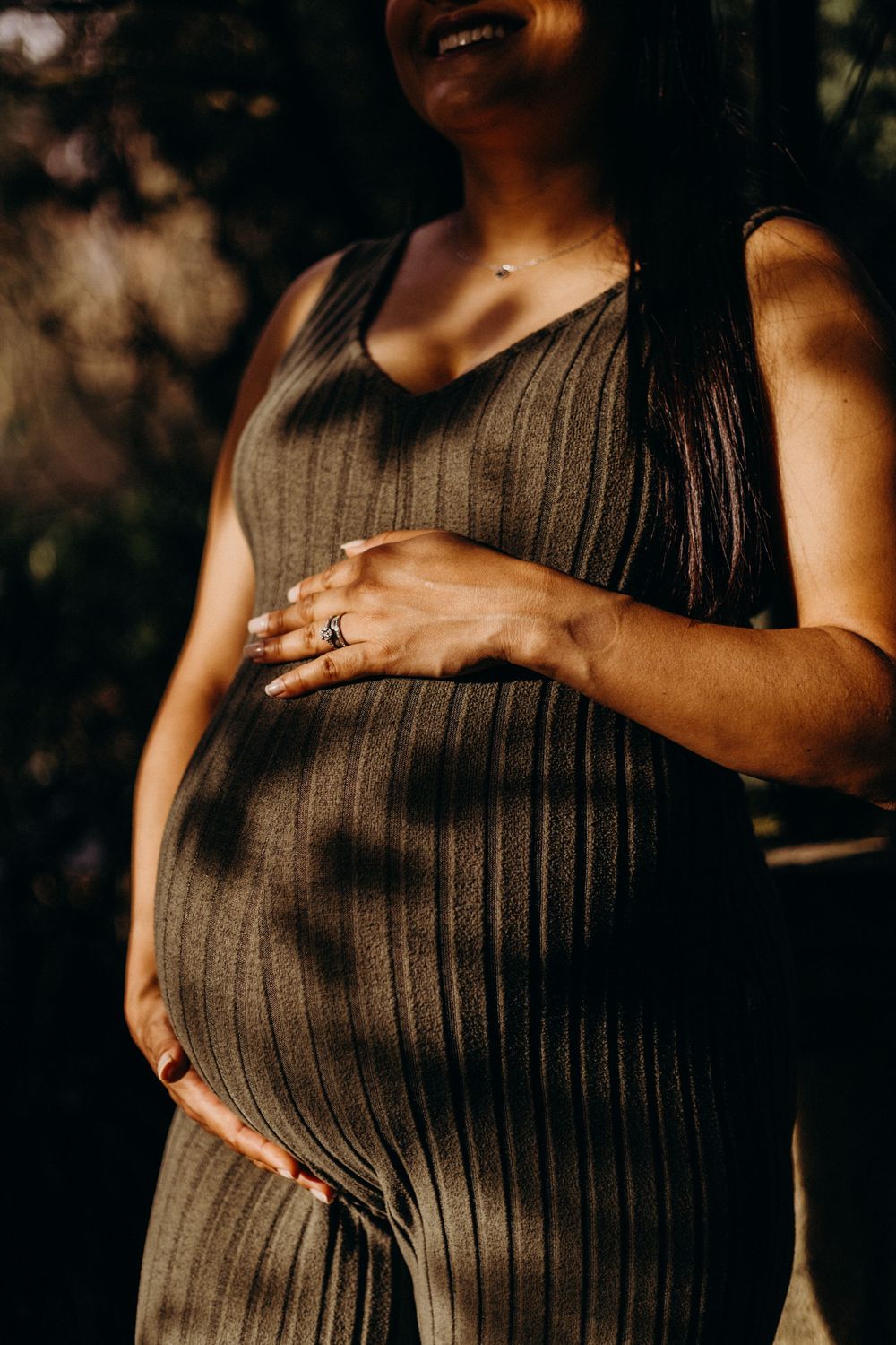 Close-up shots of pregnant belly in brown dress with hands lovingly placed on stomach.